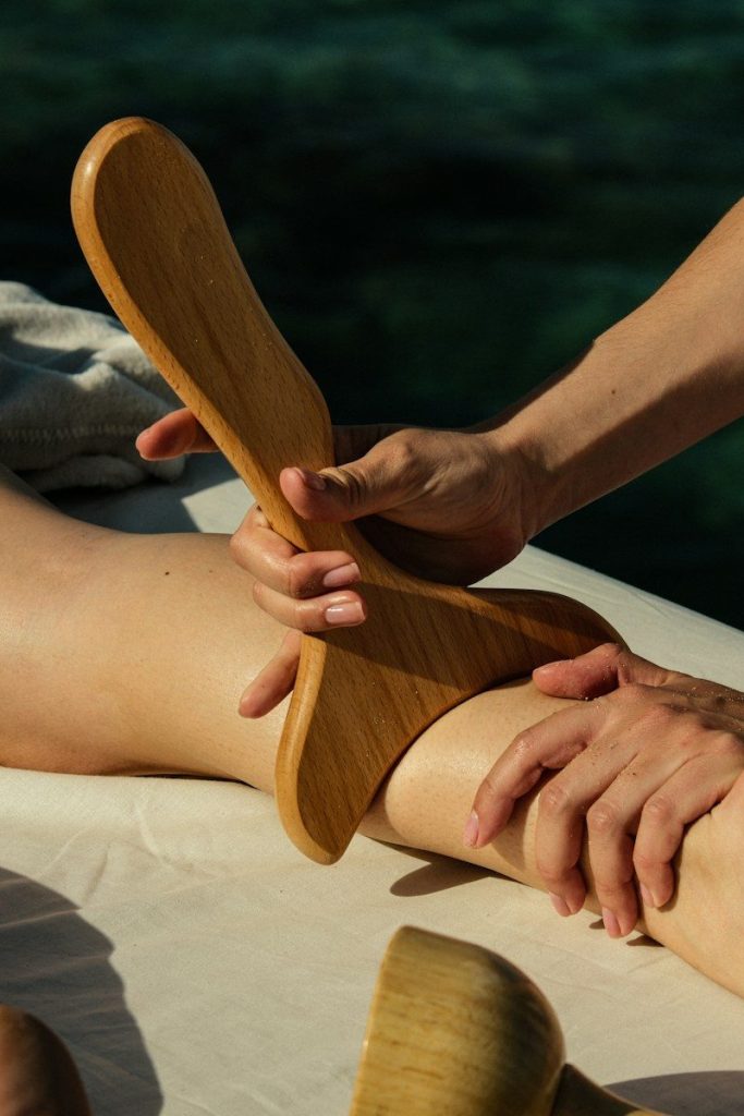 Hands using a wooden massage tool on a person's leg outdoors